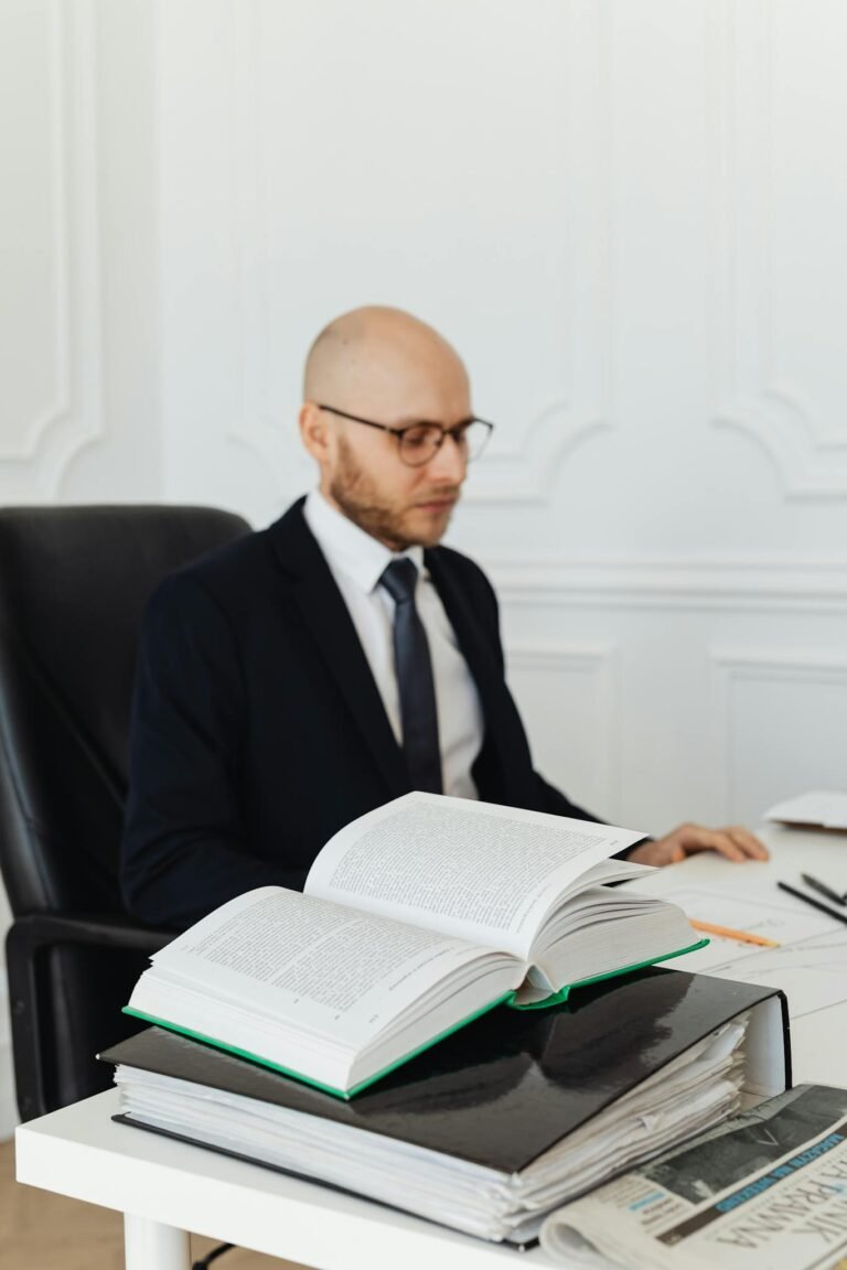 Bald businessman reading an open book in a modern office setting.